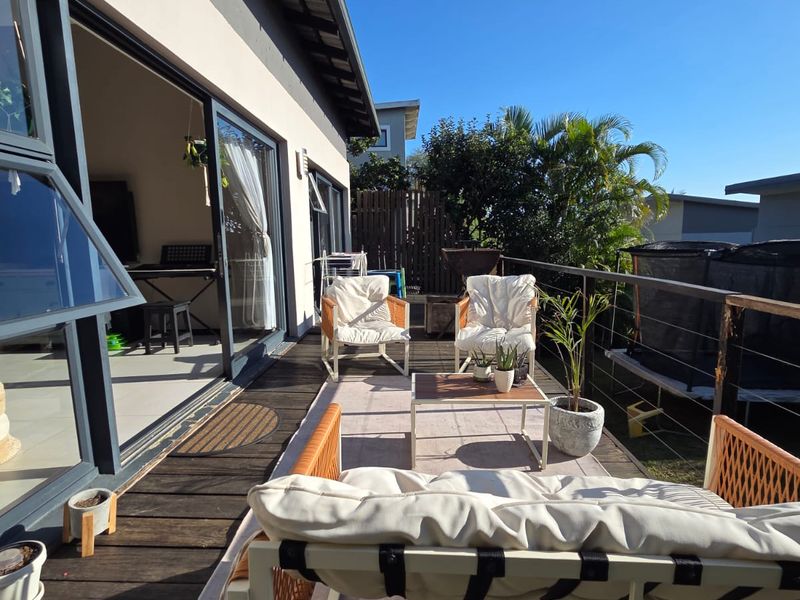An elevated timber balcony featuring sliding glass door access and metal railings, providing an outdoor living space with views of the surrounding garden.