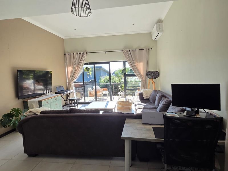 Open-plan living area featuring large format floor tiles, a split-system air conditioner, and sliding glass doors providing access to an outdoor patio.