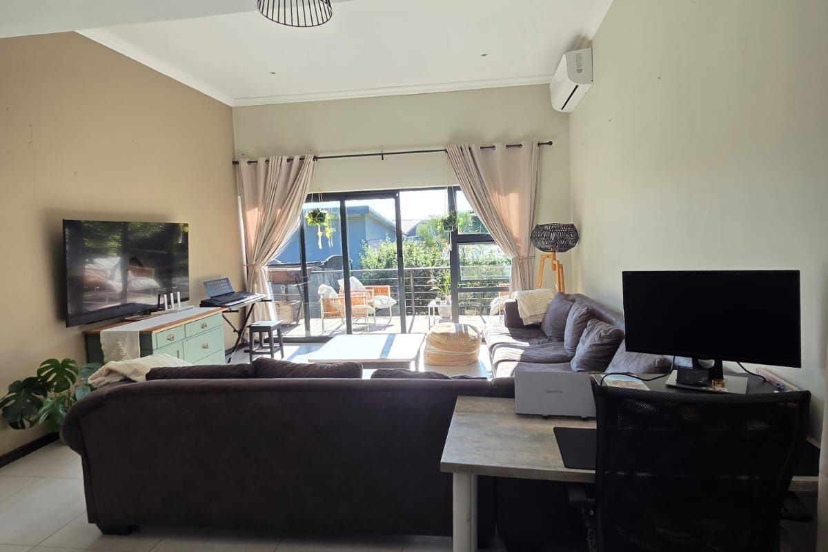 Open-plan living area featuring large format floor tiles, a split-system air conditioner, and sliding glass doors providing access to an outdoor patio.