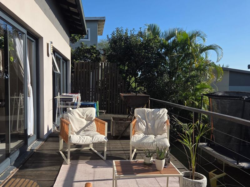 A sunny outdoor timber deck patio featuring a metal balustrade and direct access to the home through large sliding glass doors.