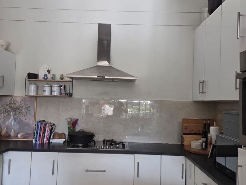 A functional kitchen featuring white cabinetry, dark stone countertops, a gas cooktop, and a stainless steel extractor fan with a neutral stone splashback.