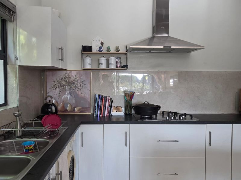 A functional kitchen featuring white cabinetry, dark stone countertops, a stainless steel extractor fan, gas hob, and tiled splashback.