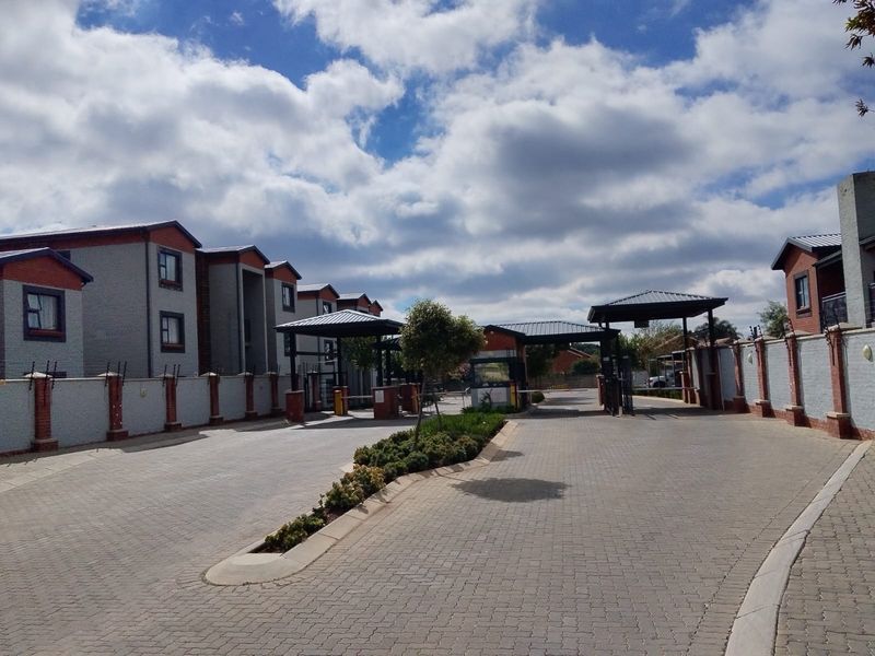 The entrance to the cluster complex features a paved driveway, security gatehouse, and perimeter walling with integrated electric fencing.
