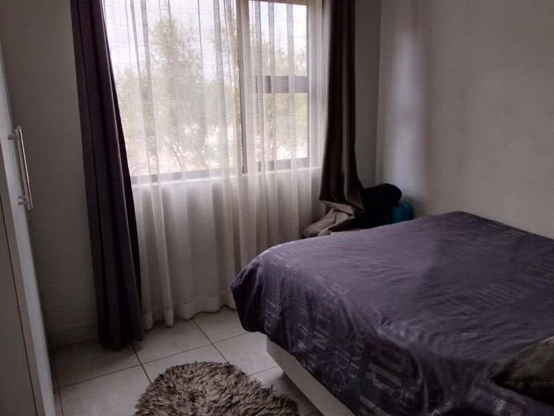 A bedroom featuring tiled flooring and a large window with curtain tracks, providing natural light.