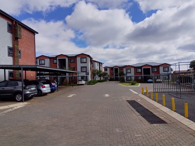 A view of the complex grounds featuring paved driveways, covered parking bays, and multi-story residential buildings with brick and plaster facades.