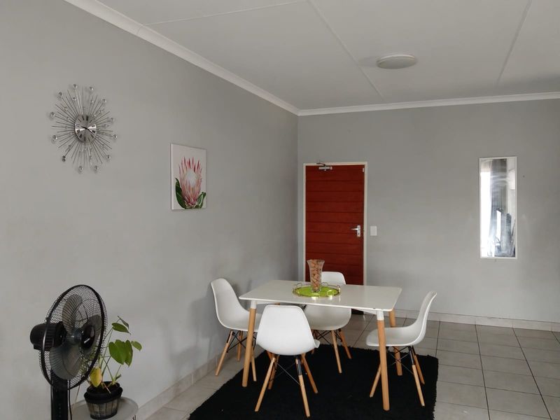 A dining area featuring neutral grey walls, tiled flooring, and a solid wood entrance door.