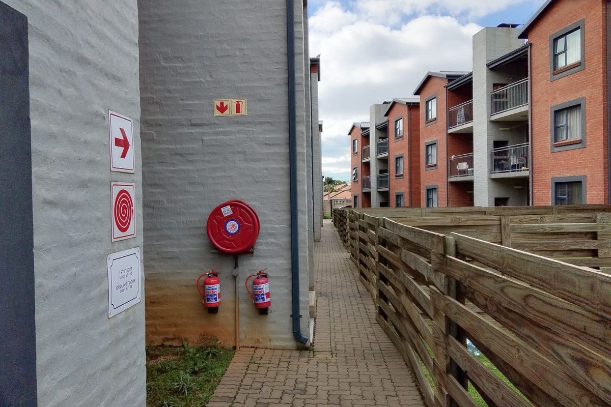 Exterior walkway between cluster units featuring paved pathways, fire safety equipment, and multi-story brick residential buildings.