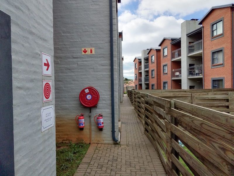 Exterior walkway between cluster units featuring paved pathways, fire safety equipment, and multi-story brick residential buildings.