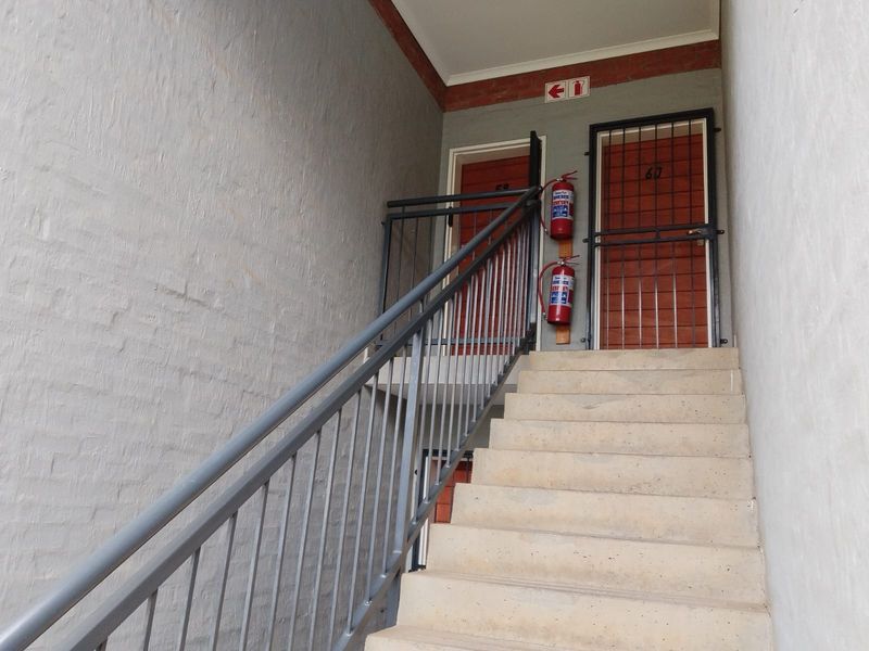 Exterior staircase leading to upper level residential units, featuring metal railings, security gates, and wall-mounted fire extinguishers.