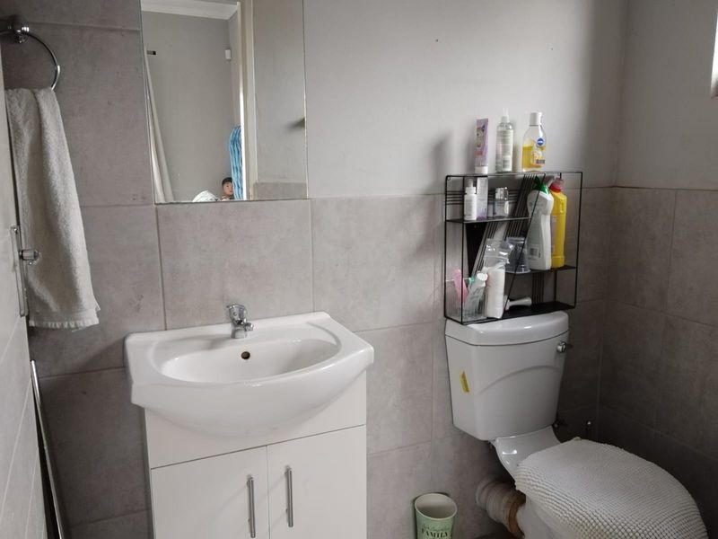 A functional bathroom featuring a wall-mounted mirror, a white vanity basin, and a standard toilet with tiled wall finishes.