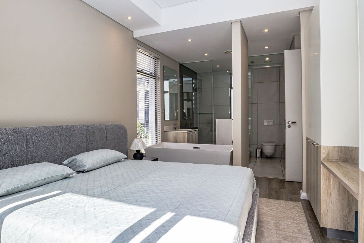 Modern bedroom featuring an open-plan en-suite bathroom with a freestanding bathtub, glass-enclosed shower, and contemporary vanity.