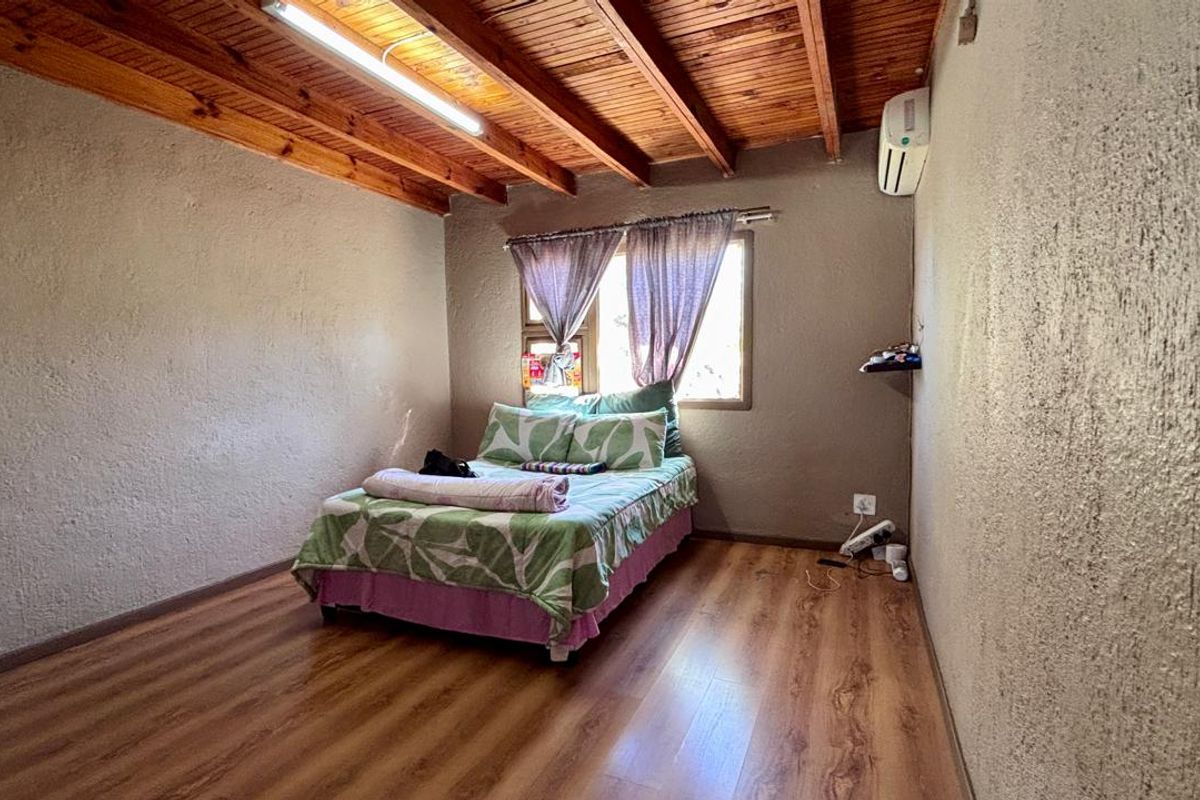 A bedroom featuring exposed timber ceiling beams, laminate flooring, and a wall-mounted air conditioning unit.