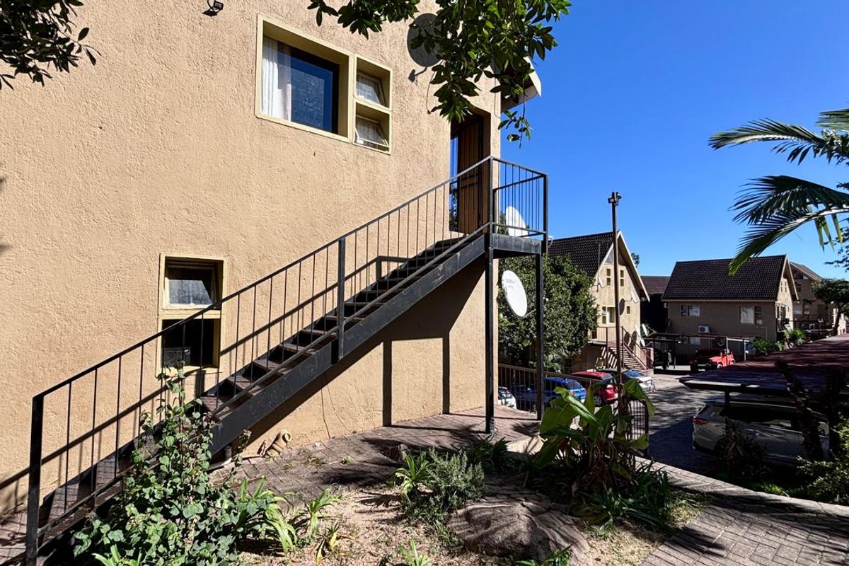 Exterior view of an apartment building featuring a metal staircase leading to an upper-level entrance, set within a residential complex.