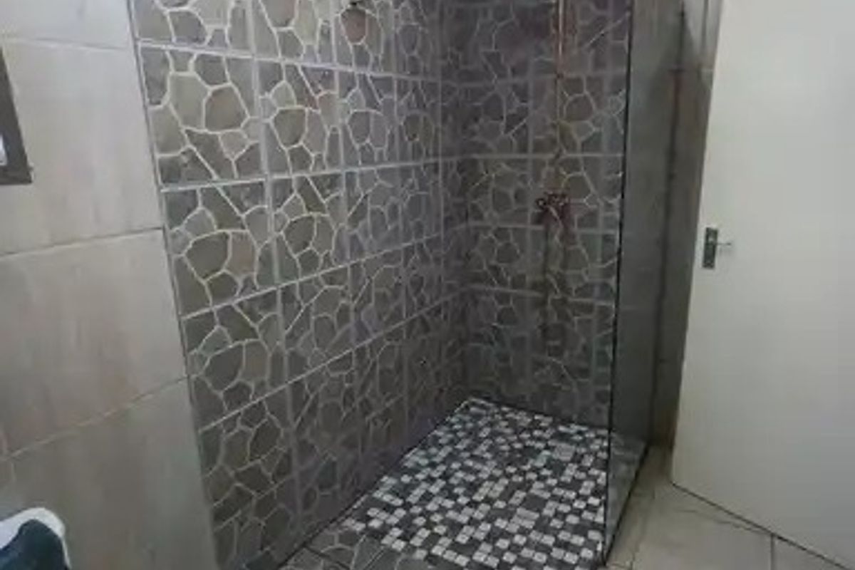 A functional bathroom featuring a walk-in shower with decorative stone-look tiling, a glass shower screen, and neutral floor tiles.