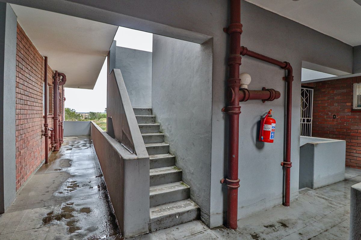 An exterior communal walkway and stairwell area featuring exposed brickwork, concrete stairs, and visible fire safety infrastructure.