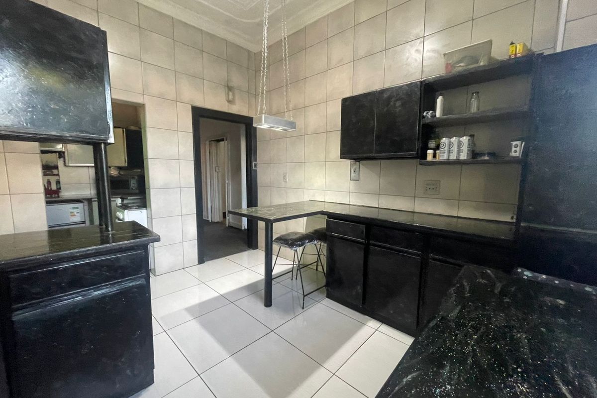A functional kitchen featuring dark built-in cabinetry, tiled walls and flooring, and a breakfast bar, with an adjoining scullery area.