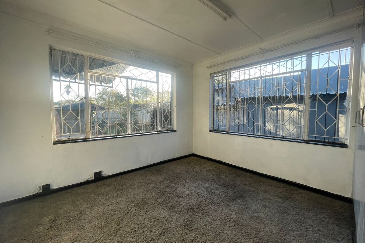 An empty bedroom featuring carpet flooring and large windows fitted with security bars, offering a blank canvas for renovation.
