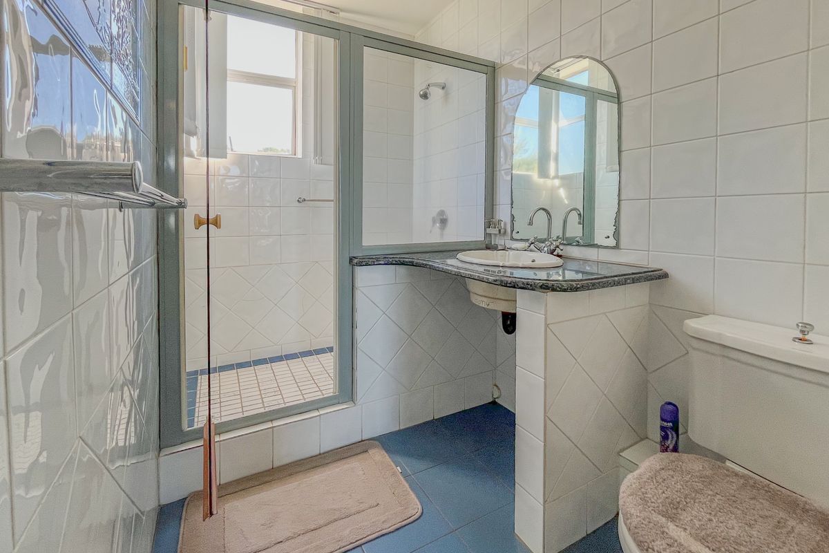 A dated bathroom featuring a tiled shower enclosure, a vanity with a stone countertop, and a standard toilet.