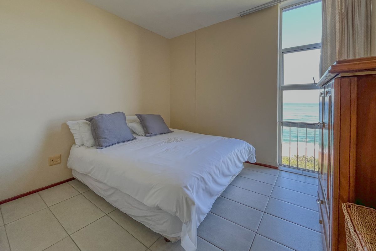 A bedroom featuring tiled flooring and a large window with direct ocean views, providing natural light and a coastal atmosphere.