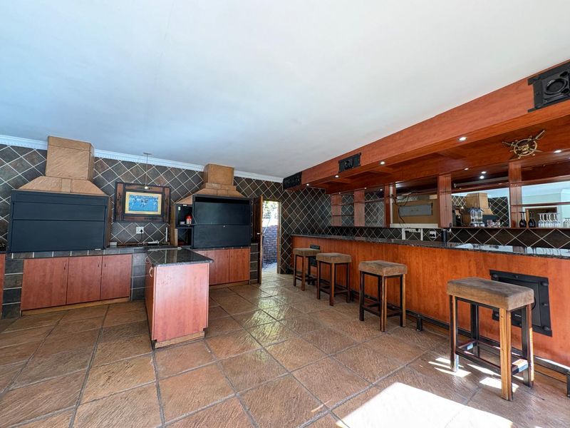 Spacious entertainment area featuring a built-in bar with granite countertops and dual built-in braai units, finished with tiled flooring throughout.