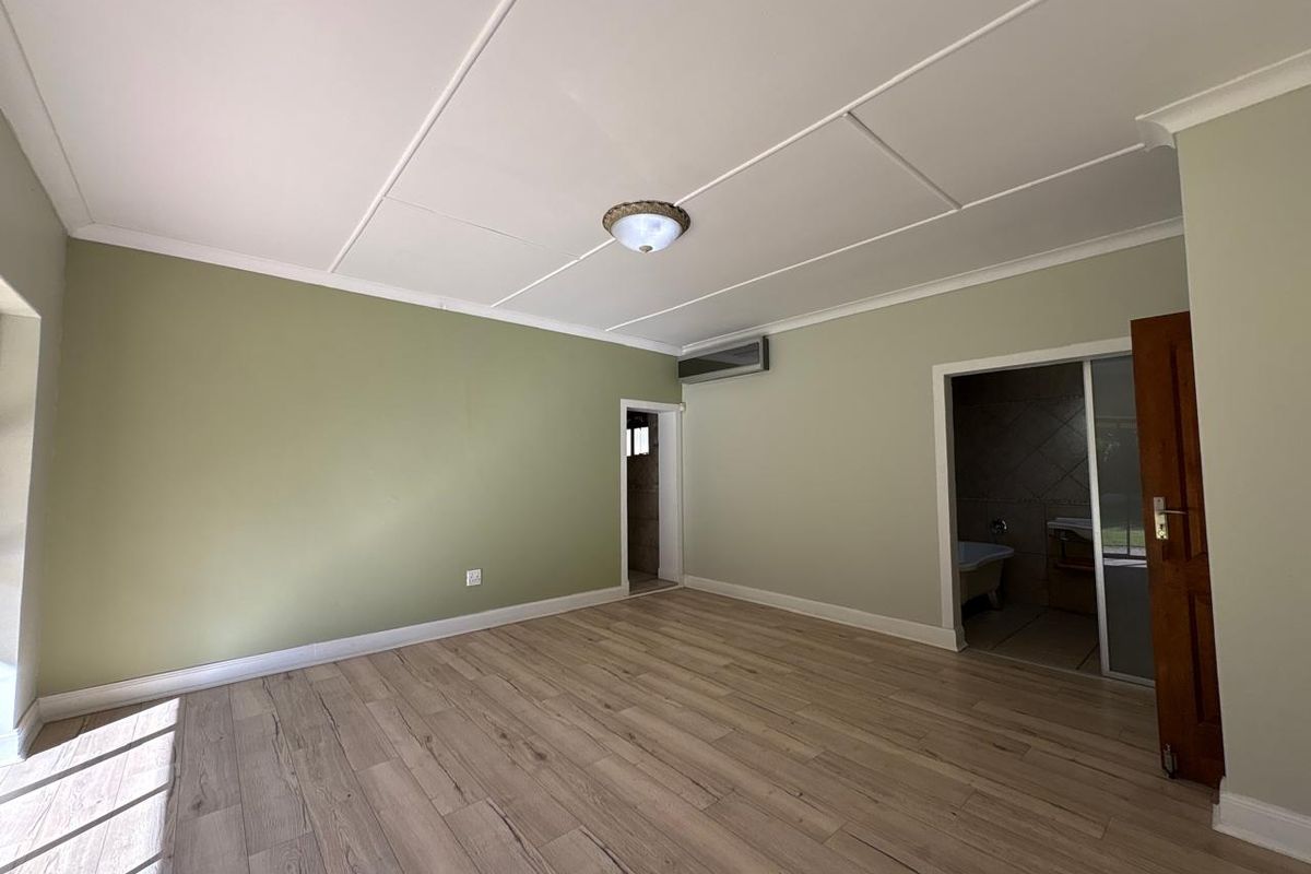 A spacious, empty bedroom featuring light-toned laminate flooring, sage green walls, and an integrated split-system air conditioning unit with an adjoining bathroom.