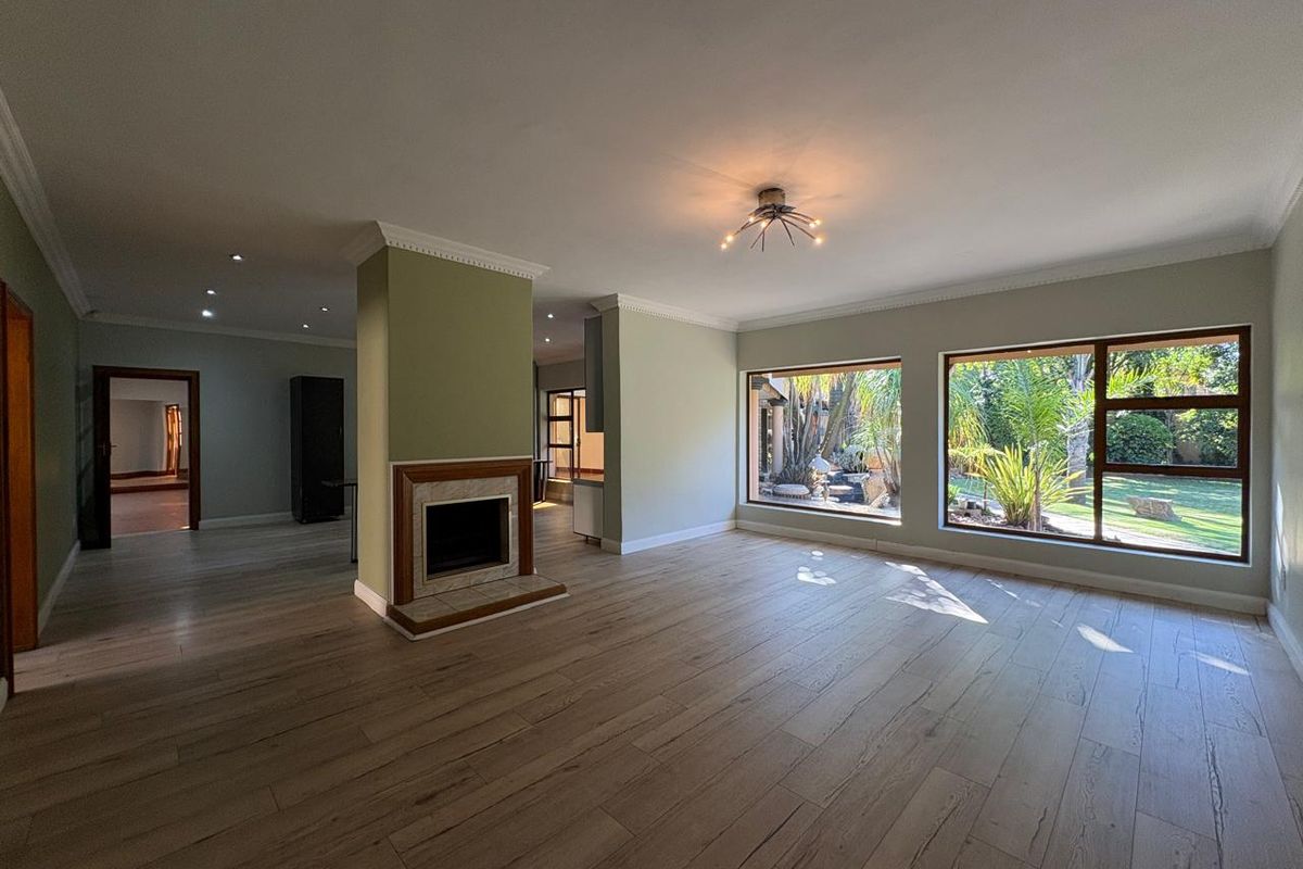 Spacious, light-filled living area featuring timber-look tile flooring, a central fireplace, and large windows overlooking the garden.