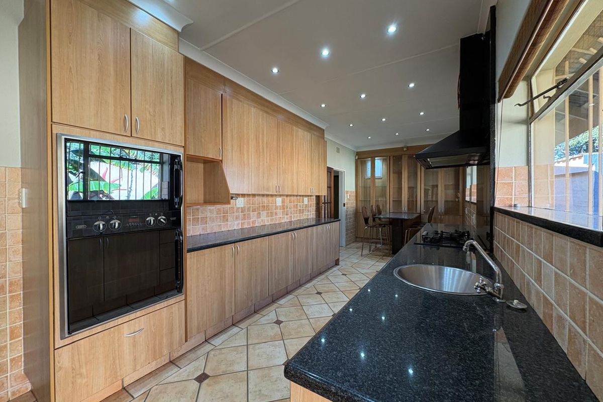 A well-maintained kitchen featuring light wood cabinetry, dark granite countertops, built-in oven, gas hob, and tiled flooring with recessed lighting.
