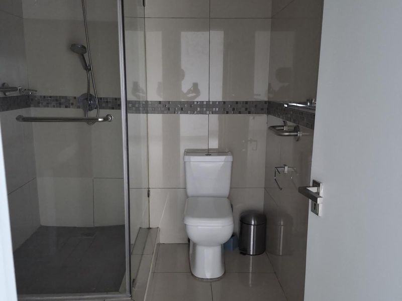 A modern bathroom featuring a glass-enclosed shower, tiled walls with decorative mosaic accents, and a standard toilet.