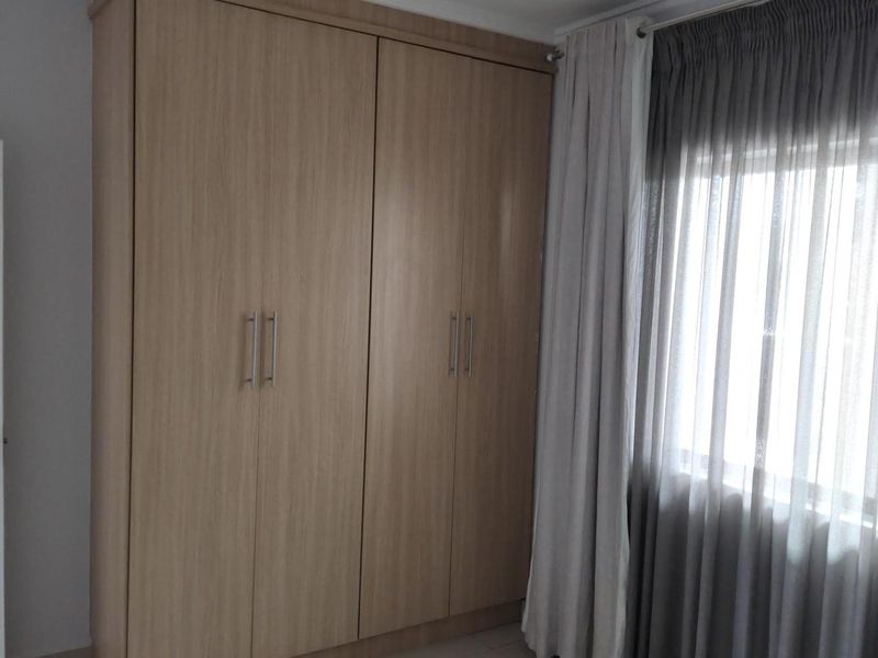 A bedroom featuring light wood-finish built-in cupboards and tiled flooring, complemented by neutral curtains.