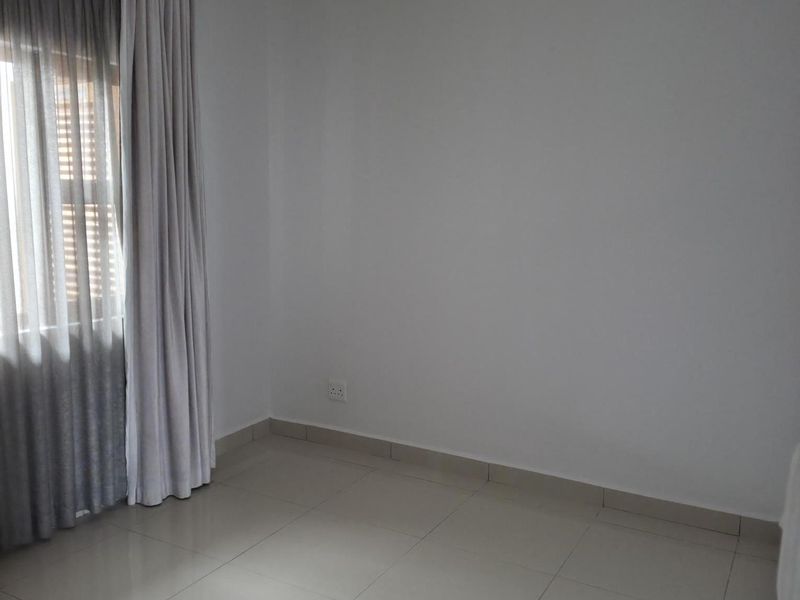 A bright, empty bedroom featuring neutral tiled flooring, recessed ceiling lighting, and floor-to-ceiling curtains.