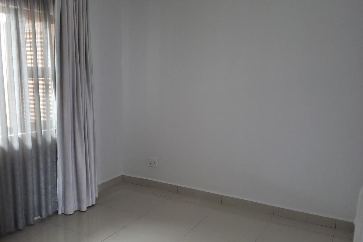 A bright, empty bedroom featuring neutral tiled flooring, recessed ceiling lighting, and floor-to-ceiling curtains.