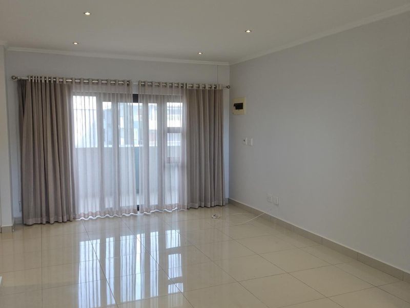 A bright and spacious open-plan living area featuring polished porcelain floor tiles, recessed downlighting, and large sliding glass doors leading to a balcony.