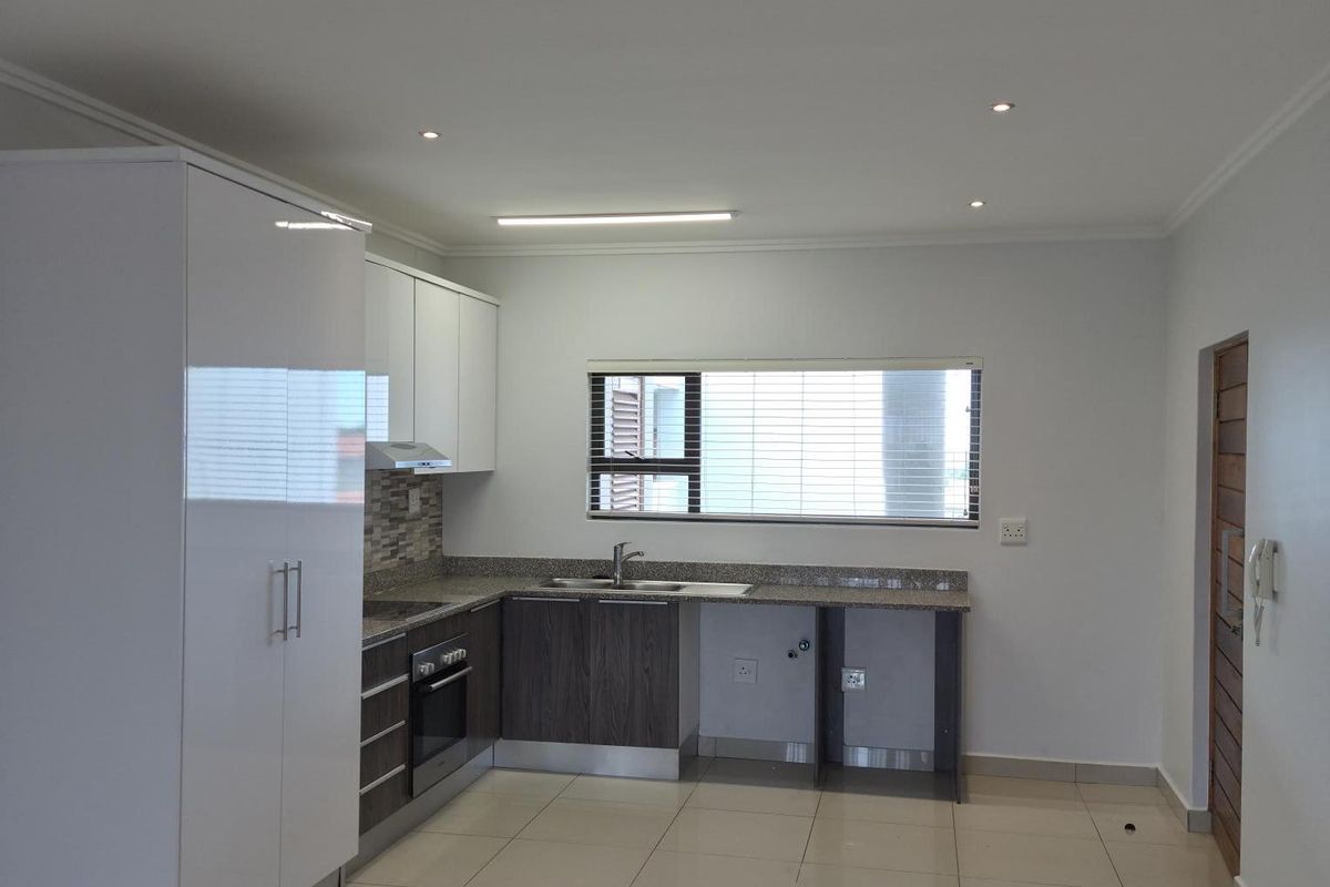 Modern kitchen featuring sleek white and dark wood cabinetry, granite countertops, built-in oven, extractor fan, and tiled flooring in an open-plan layout.