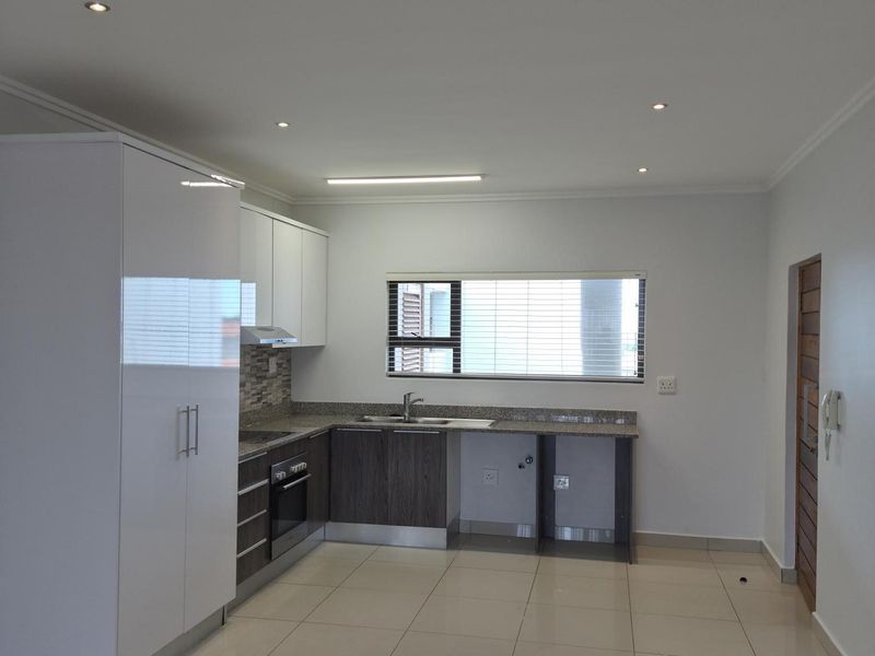 Modern kitchen featuring sleek white and dark wood cabinetry, granite countertops, built-in oven, extractor fan, and tiled flooring in an open-plan layout.