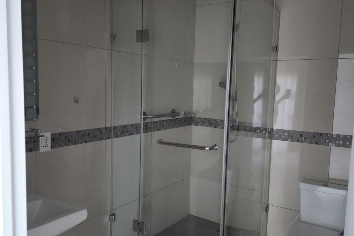 A modern bathroom featuring a glass-enclosed shower, pedestal sink, and toilet with neutral wall and floor tiling.