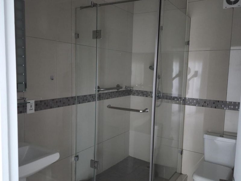 A modern bathroom featuring a glass-enclosed shower, pedestal sink, and toilet with neutral wall and floor tiling.