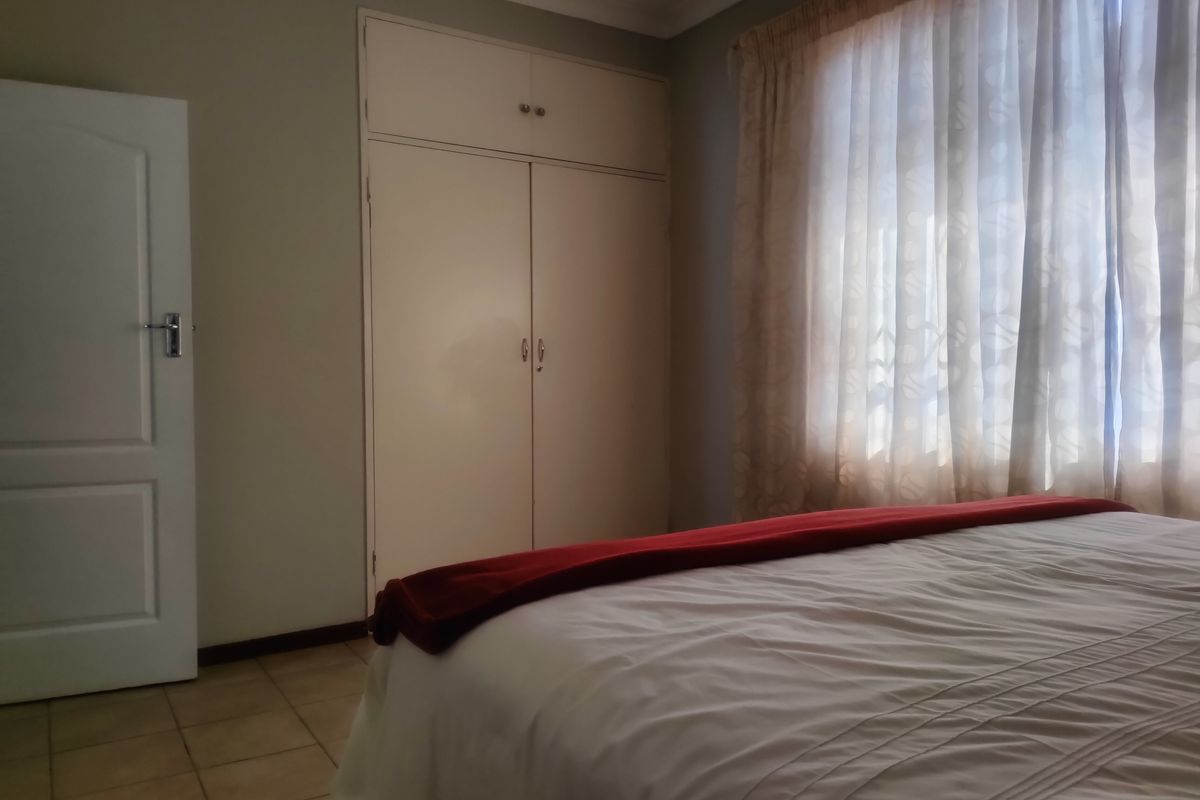 A bedroom featuring built-in cupboards, tiled flooring, and a coved ceiling, providing a functional and neutral space.