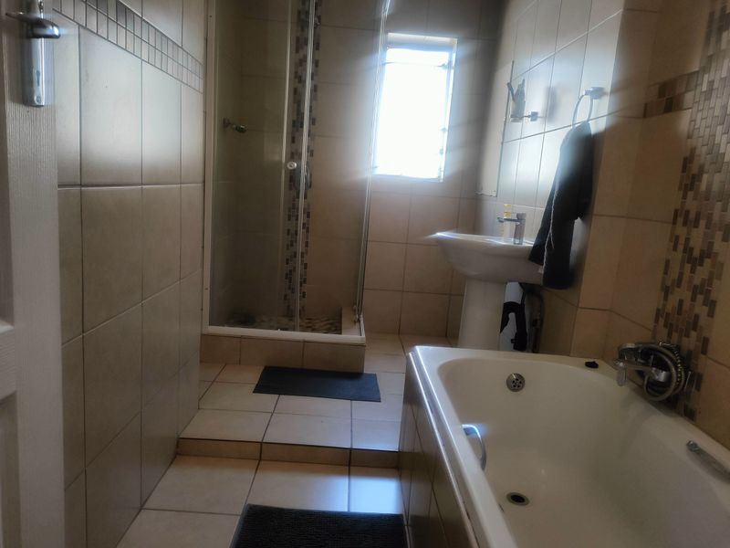 A functional bathroom featuring a shower enclosure, pedestal basin, and bathtub with neutral wall and floor tiling.