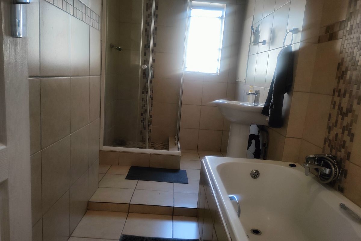A functional bathroom featuring a shower enclosure, pedestal basin, and bathtub with neutral wall and floor tiling.