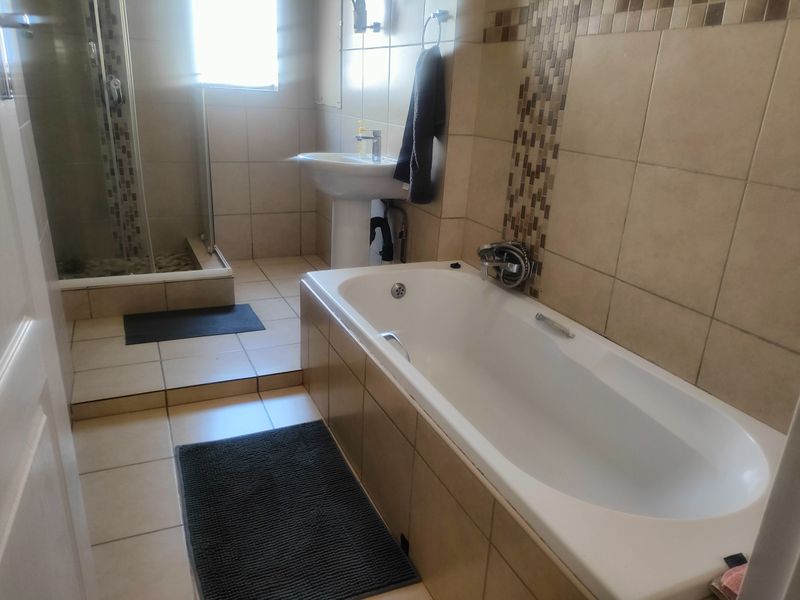 A functional bathroom featuring a pedestal basin, a built-in bathtub, and a separate glass-enclosed shower with neutral wall and floor tiling.
