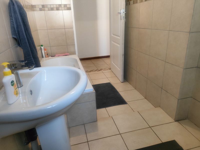 A functional bathroom featuring a pedestal basin, built-in bathtub, and neutral ceramic tiling throughout the walls and floor.