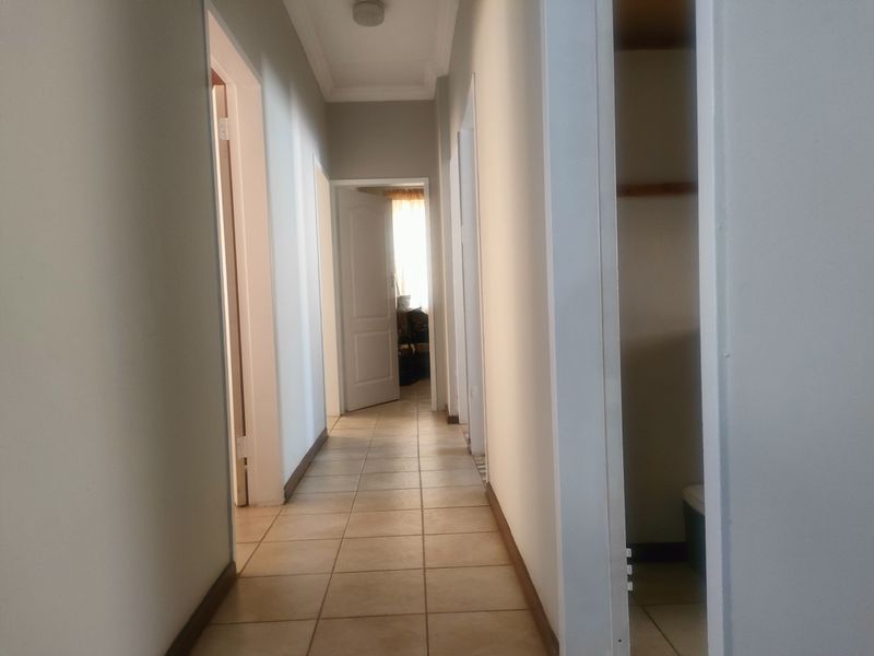A clean, neutral hallway featuring tiled flooring, coving, and access to multiple rooms, including a built-in storage cupboard.