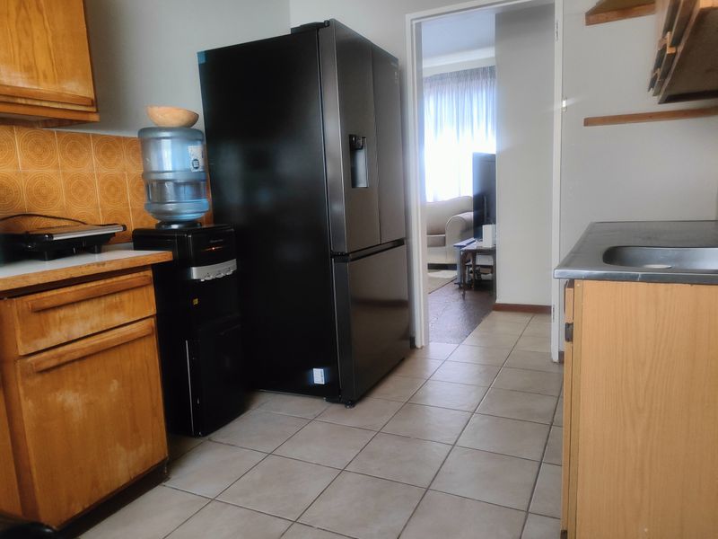 A functional kitchen area featuring wooden cabinetry, tiled backsplash, and tiled flooring, providing a practical layout with direct access to the adjacent living space.
