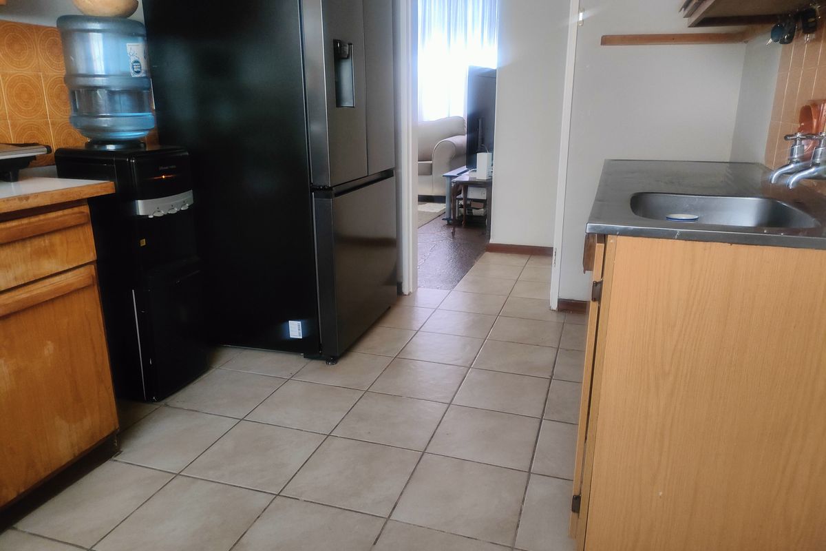A functional kitchen area featuring tiled flooring, built-in wooden cabinetry, and a stainless steel sink, offering potential for modernization and aesthetic updates.