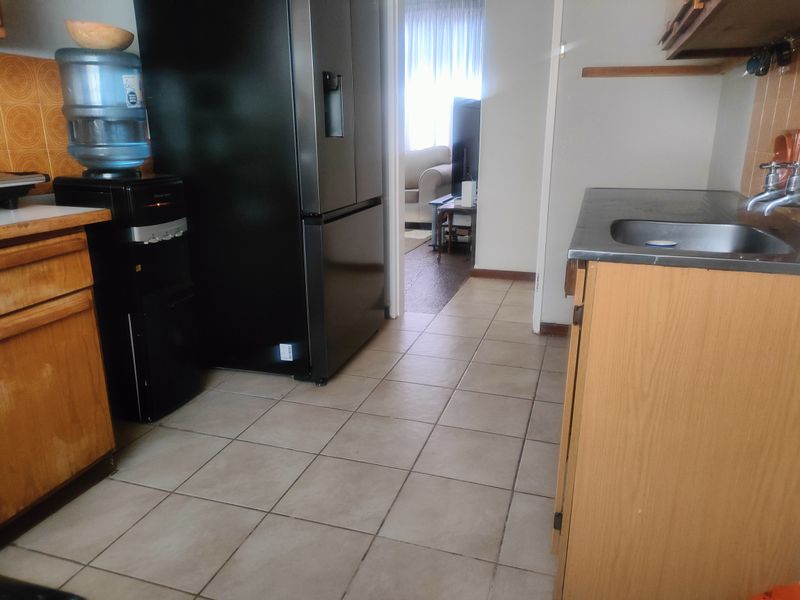 A functional kitchen area featuring tiled flooring, built-in wooden cabinetry, and a stainless steel sink, offering potential for modernization and aesthetic updates.
