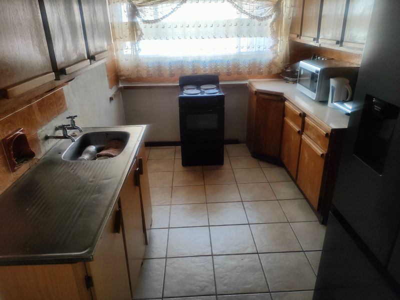 A dated kitchen featuring wooden cabinetry, a stainless steel sink, tiled flooring, and a freestanding stove, offering potential for modernization.