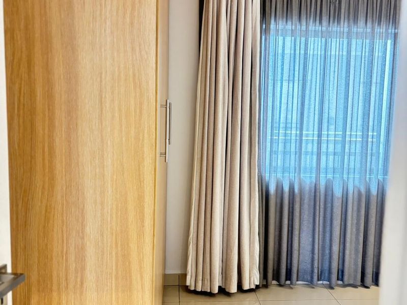 A bedroom featuring light-toned tiled flooring and a large built-in wooden wardrobe, complemented by floor-to-ceiling curtains.