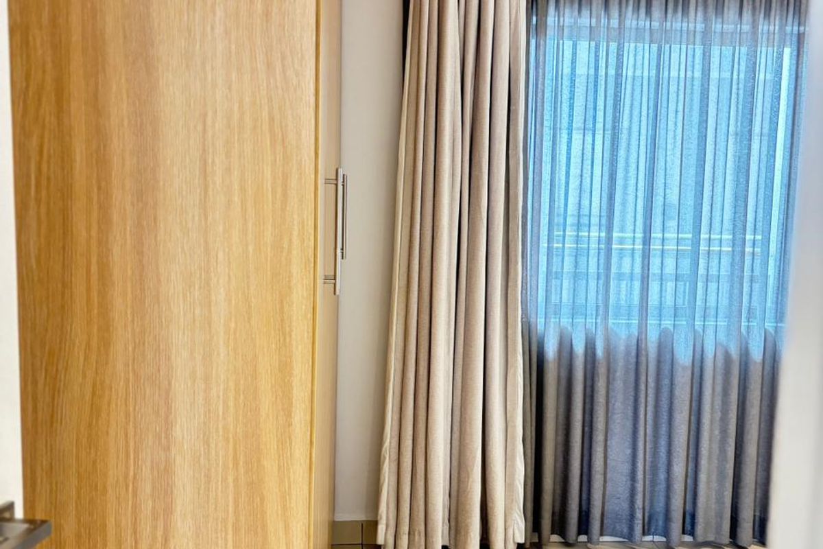 A bedroom featuring light-toned tiled flooring and a large built-in wooden wardrobe, complemented by floor-to-ceiling curtains.