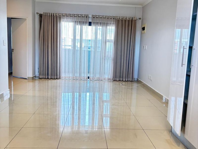 Spacious open-plan living area featuring polished porcelain floor tiles, recessed downlighting, and large sliding glass doors leading to a balcony.