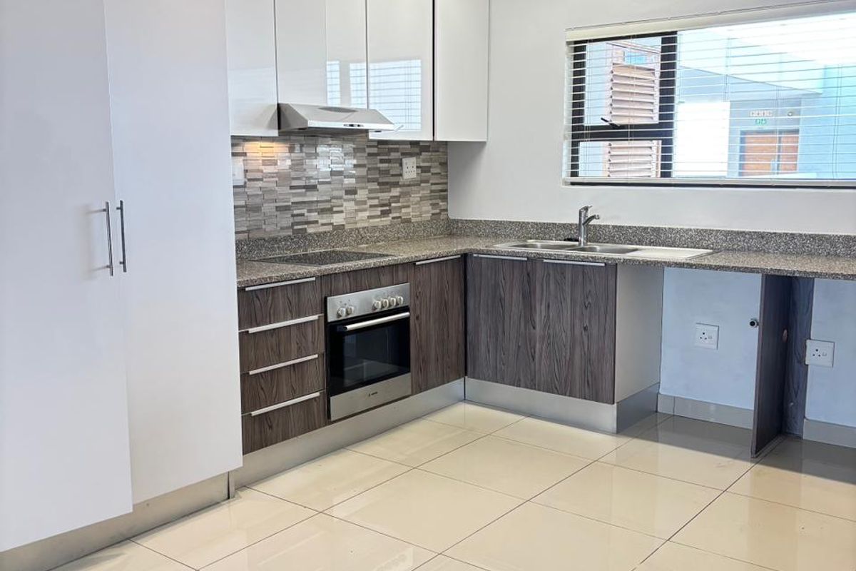 Modern kitchen featuring high-gloss white upper cabinetry, wood-grain lower cabinets, granite countertops, tiled backsplash, and built-in oven with extractor fan.